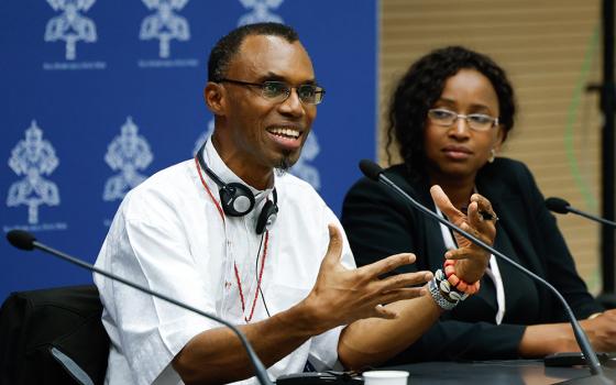 Jesuit Fr. Agbonkhianmeghe Orobator, dean of the Jesuit School of Theology at Santa Clara University in California, speaks during a briefing about the assembly of the Synod of Bishops at the Vatican Oct. 17. Sheila Leocádia Pires, secretary of the synod's information commission, looks on. (CNS/Lola Gomez)